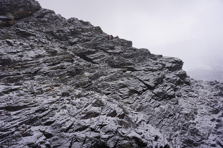 Rocky mountain terrain covered in snow with climbers visible.