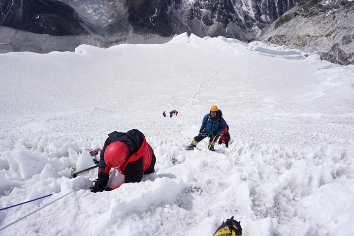 Climbers ascending a snowy mountain slope using ropes.