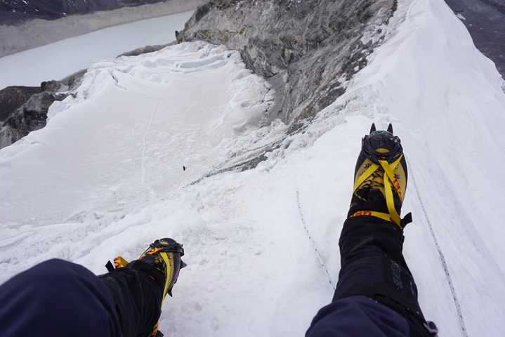 Close-up of a climber’s boots on a snowy mountain ledge.
