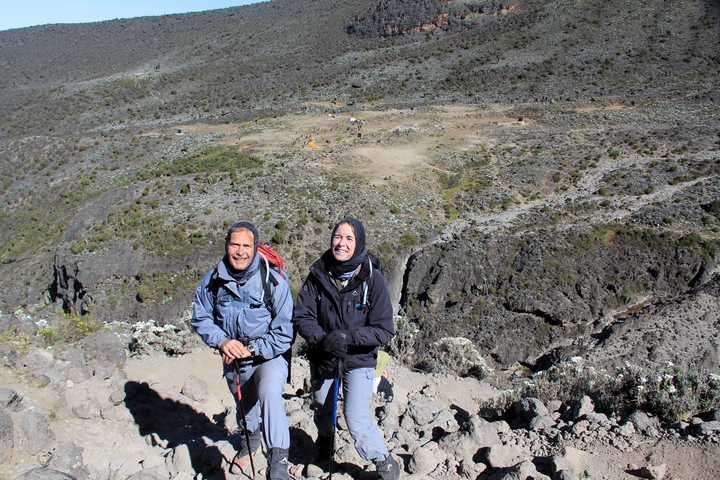 Two hikers smiling on a rocky terrain with a distant view