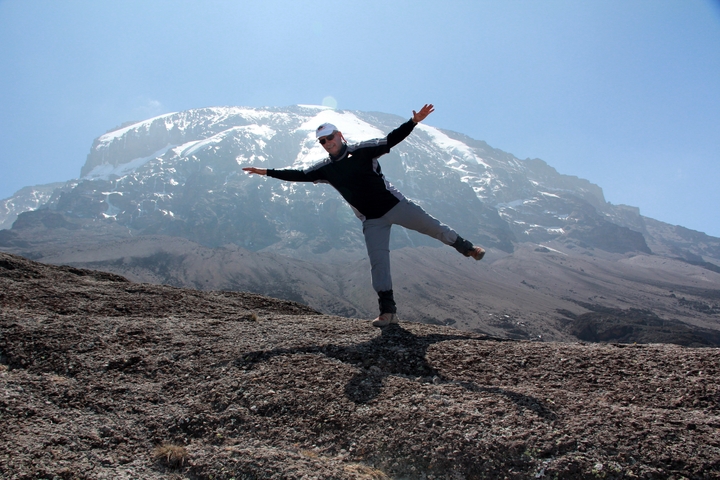       A hiker posing with arms outstretched, with Mount Kilimanjaro in the background.
  
