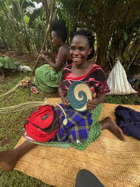       A woman sitting on a mat holding a woven item.
  