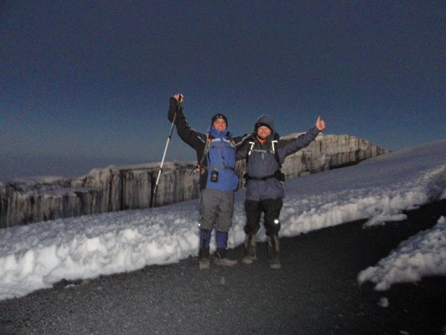 Two people in hiking gear posing on a snowy mountain.