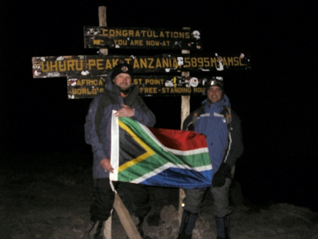 Two people holding a flag at Uhuru Peak, Mount Kilimanjaro at night