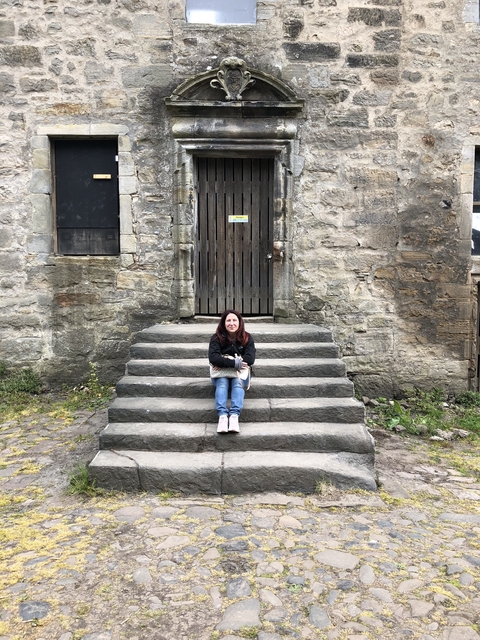 Smiling person sitting on stairs outside a stone building.