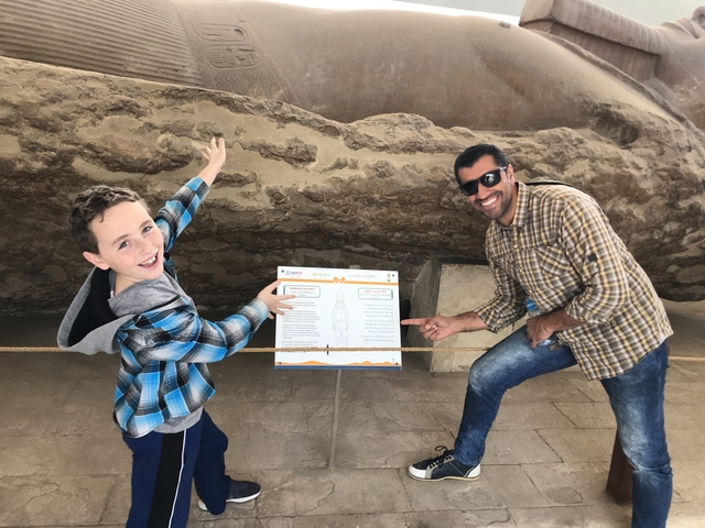       Two people pointing at an educational sign next to an archaeological site.
  