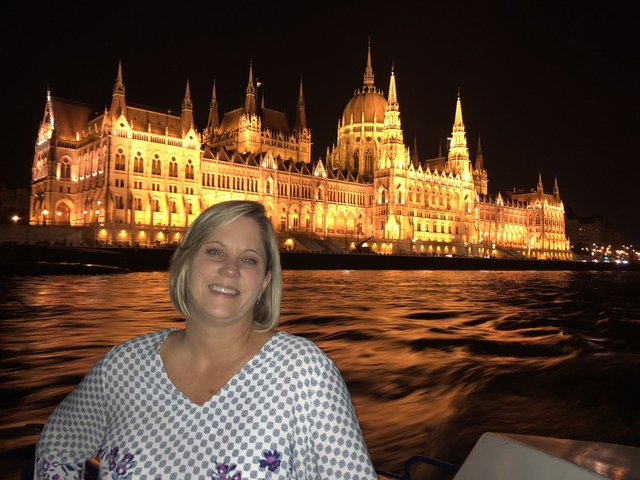 Woman smiling with the illuminated Hungarian Parliament Building at night.