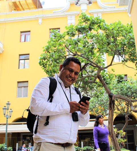       Man smiling while checking his phone against a yellow wall.
  