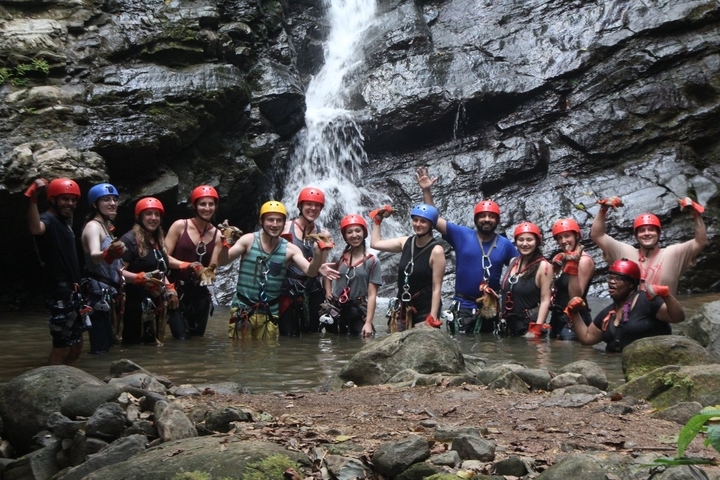 Group of people posing in front of a waterfall.