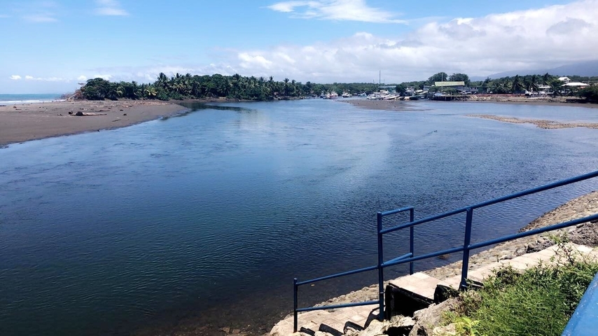 River with a town and forested area in the background under a blue sky.