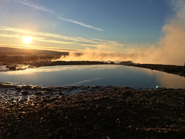       Steam rising from geothermal hot springs with sunset in the background.
  