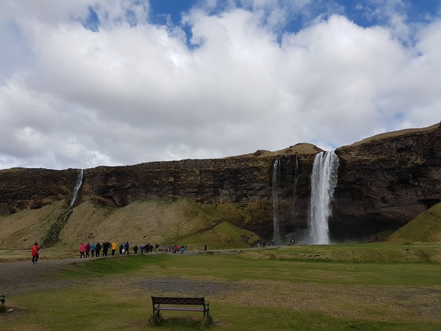       People walking towards a waterfall known as Skogafoss.
  