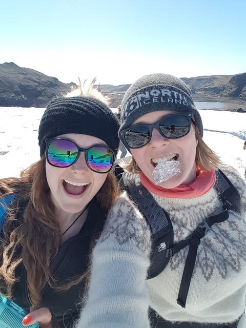       Two women smiling with winter clothing, one holding a foil-covered snack.
  
