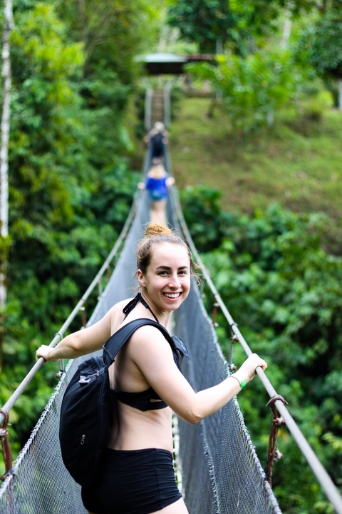 Woman smiling on a suspension bridge in a lush green forest.