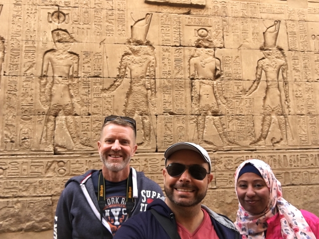 Three people posing in front of a wall with Egyptian carvings.