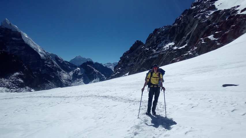 A hiker with poles walking in a snowy mountainous landscape.