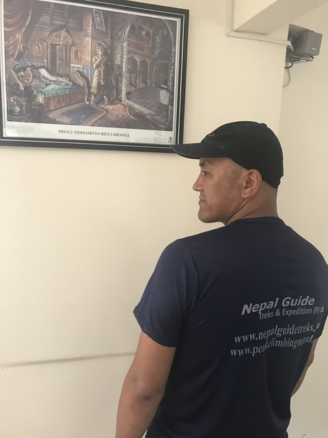 Side view of a man wearing a cap, standing indoors with a wall feature behind.