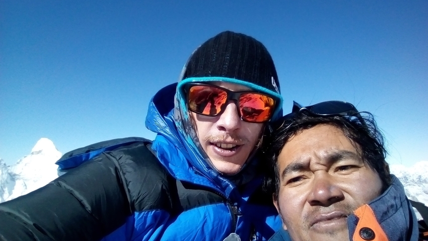 Two people wearing winter clothes taking a selfie in a snowy mountain setting.