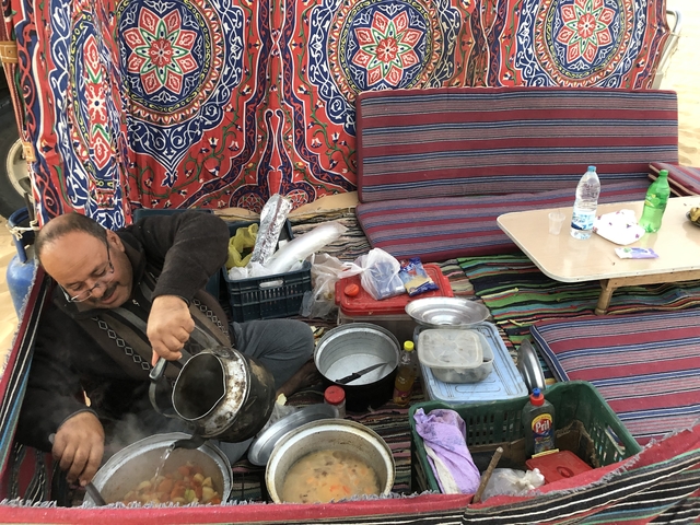 Man preparing food in a tent-like setup with colorful textiles.