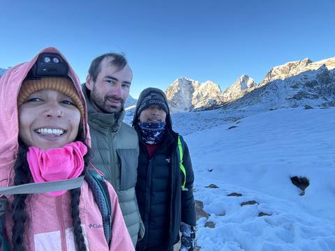       Three people smiling with snowy peaks behind.
  
