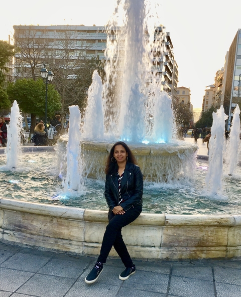       Person posing in front of a fountain in a city square.
  