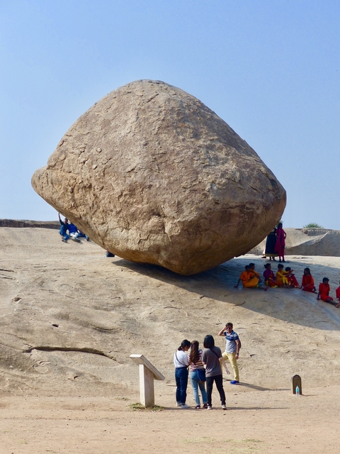       Large boulder with tourists sitting below it.
  