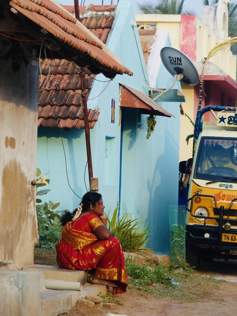       Woman sitting near a blue wall and auto rickshaw.
  
