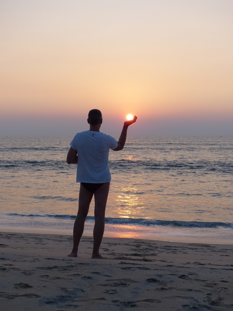       Man standing in the ocean holding the setting sun.
  