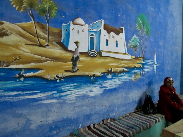       Person sitting against a painted mural of a rural landscape.
  