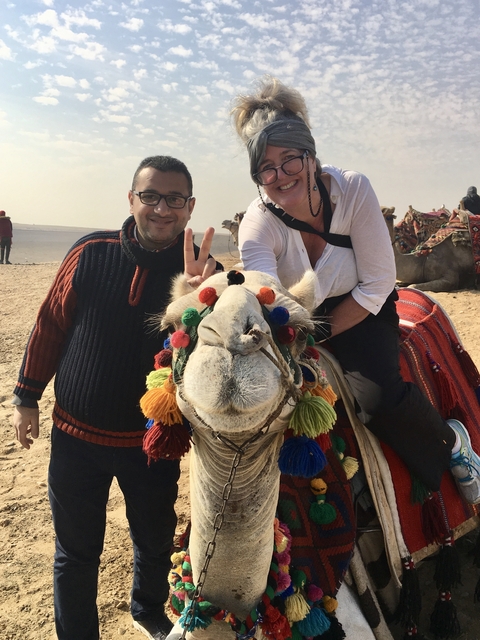       People posing on a camel beautifully decorated with colorful threads.
  