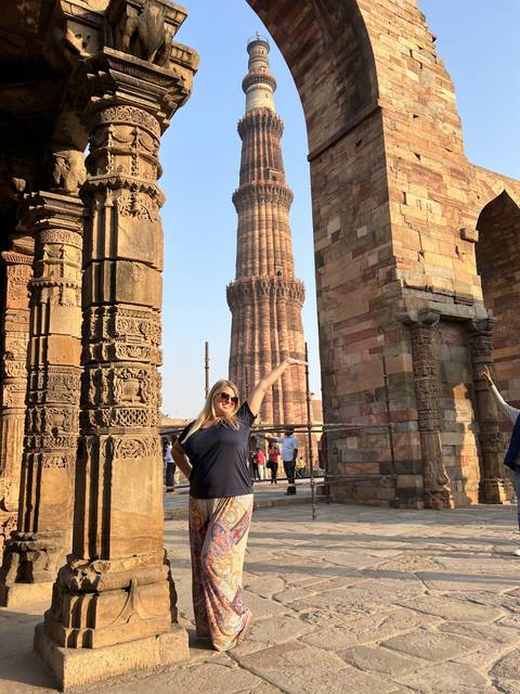 Woman joyfully posing by the Qutub Minar, a historical minaret.