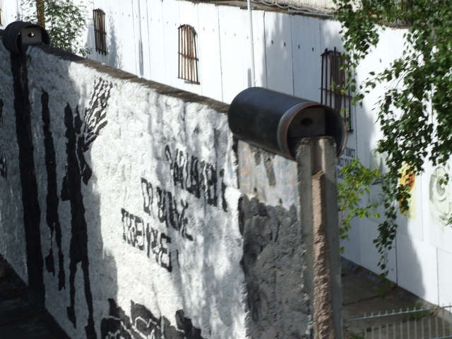 Part of the Berlin Wall with text and trees in the background.