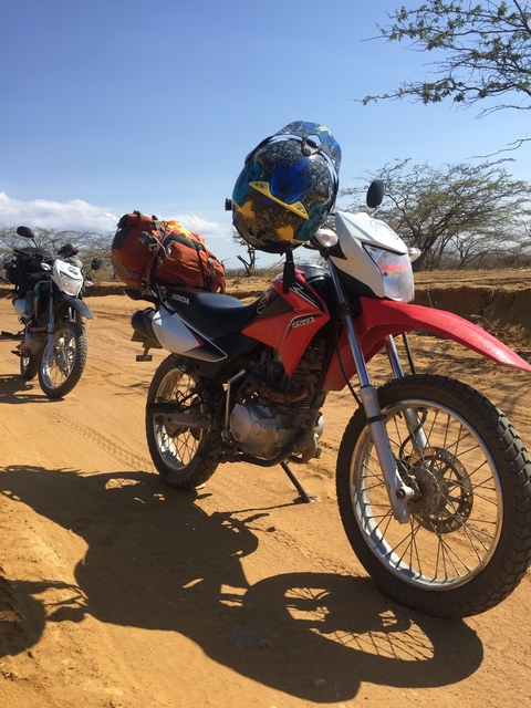       Motorcycles parked on a dusty road with travel gear.
  