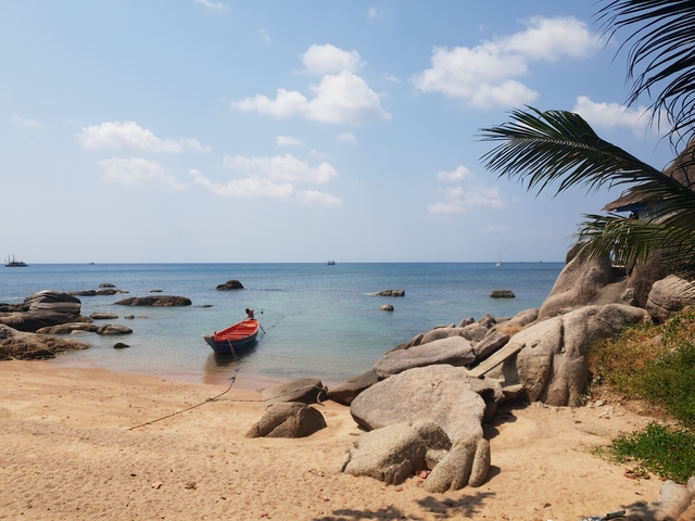 Serene beach with a boat on a calm sea and a clear blue sky.