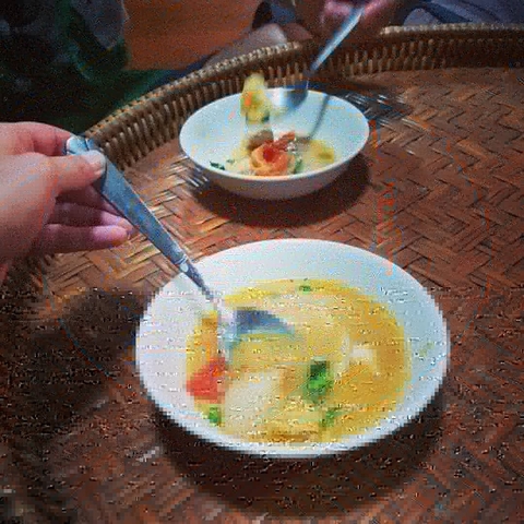 Blurry image of a person holding a spoon near a bowl of soup.