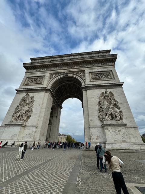       The Arc de Triomphe with people around, shot against a blue sky.
  