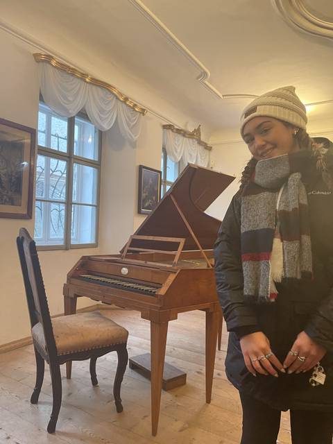 Person standing next to a historic wooden piano inside a room.