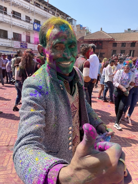 People celebrating a colorful festival, likely Holi, with vibrant colors on faces.