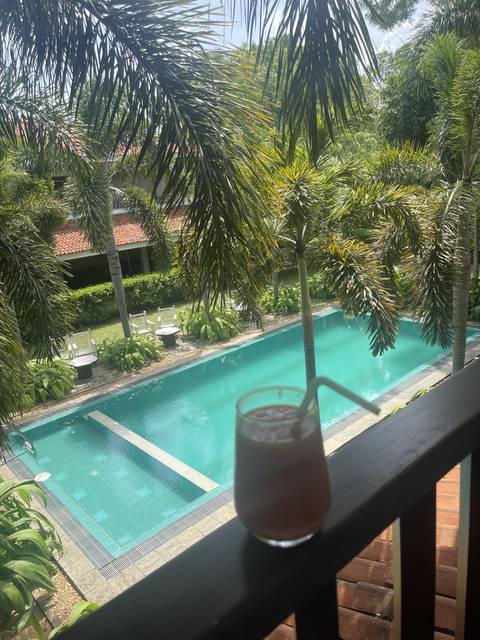 A tropical pool view with a glass of juice in the foreground.
