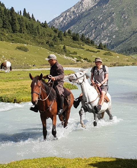 Two people riding horses across a small river