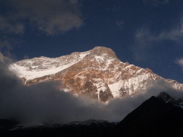       Sunlit Himalayan peak partially hidden by rolling clouds.
  