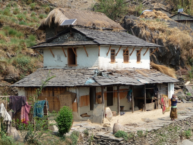       Traditional stone and wood Nepalese house with slate roof set on a hillside.
  