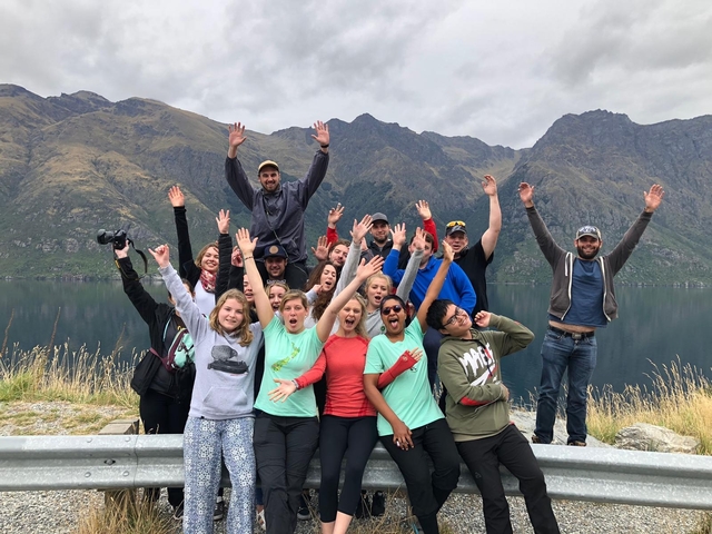 Group of people celebrating with raised hands in a scenic mountainous area.