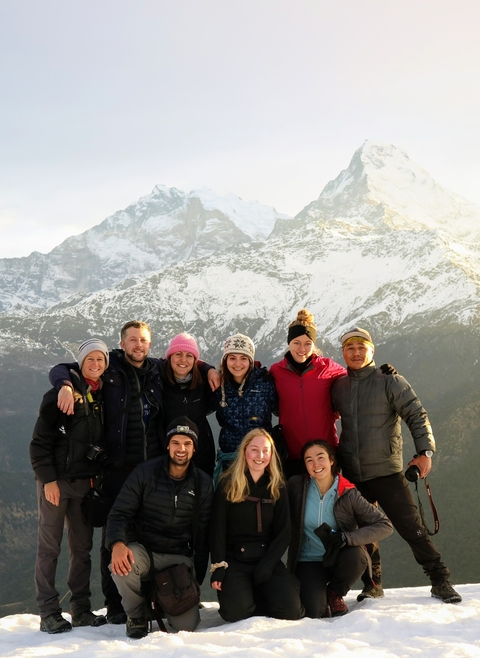 Group of people posing happily with snow-capped mountains in the background.