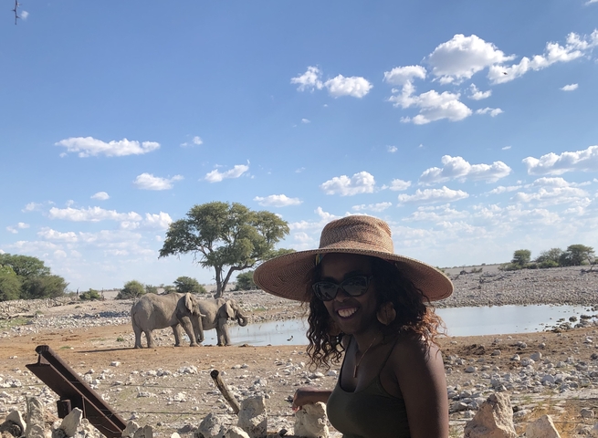 Woman wearing a hat with elephants in the background.