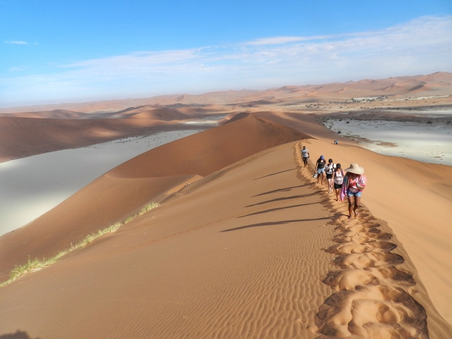 Group of people walking on sand dunes.