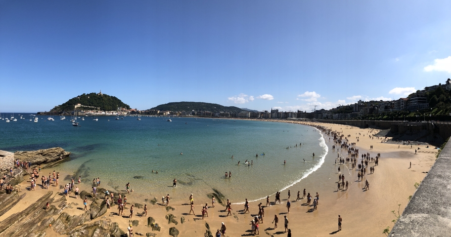 Panoramic view of a crowded beach with hills in the background.