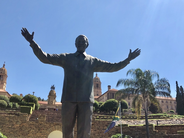       Statue of a man with arms outstretched in front of a historic building.
  