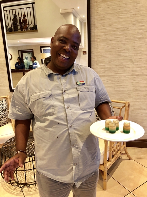       Man holding a tray of colorful drinks indoors.
  