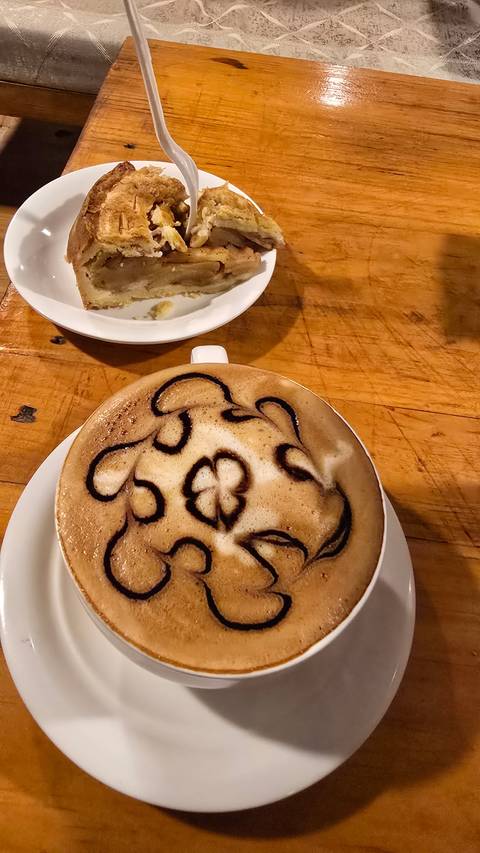       Coffee with intricate latte art and a slice of pie on a wooden table.
  